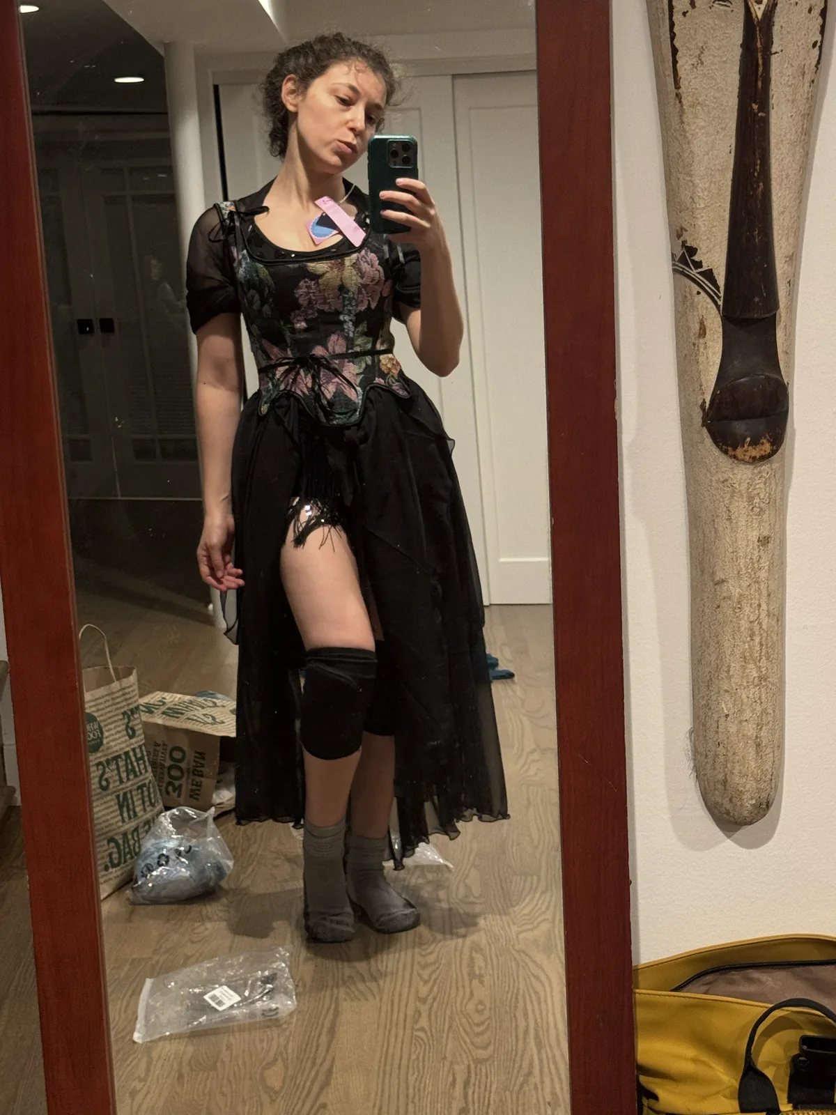 Mirror selfie wearing a floral black corset with a short black skirt, sheer train, and knee pads.