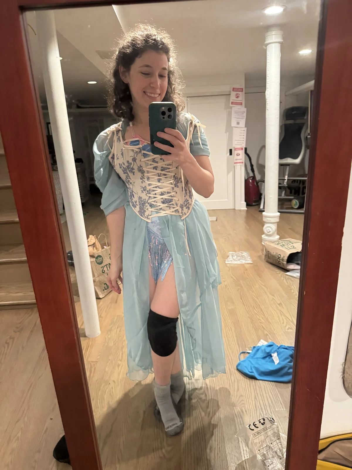 Mirror selfie wearing a pale blue corset with a high-low light blue skirt and one black knee pad.