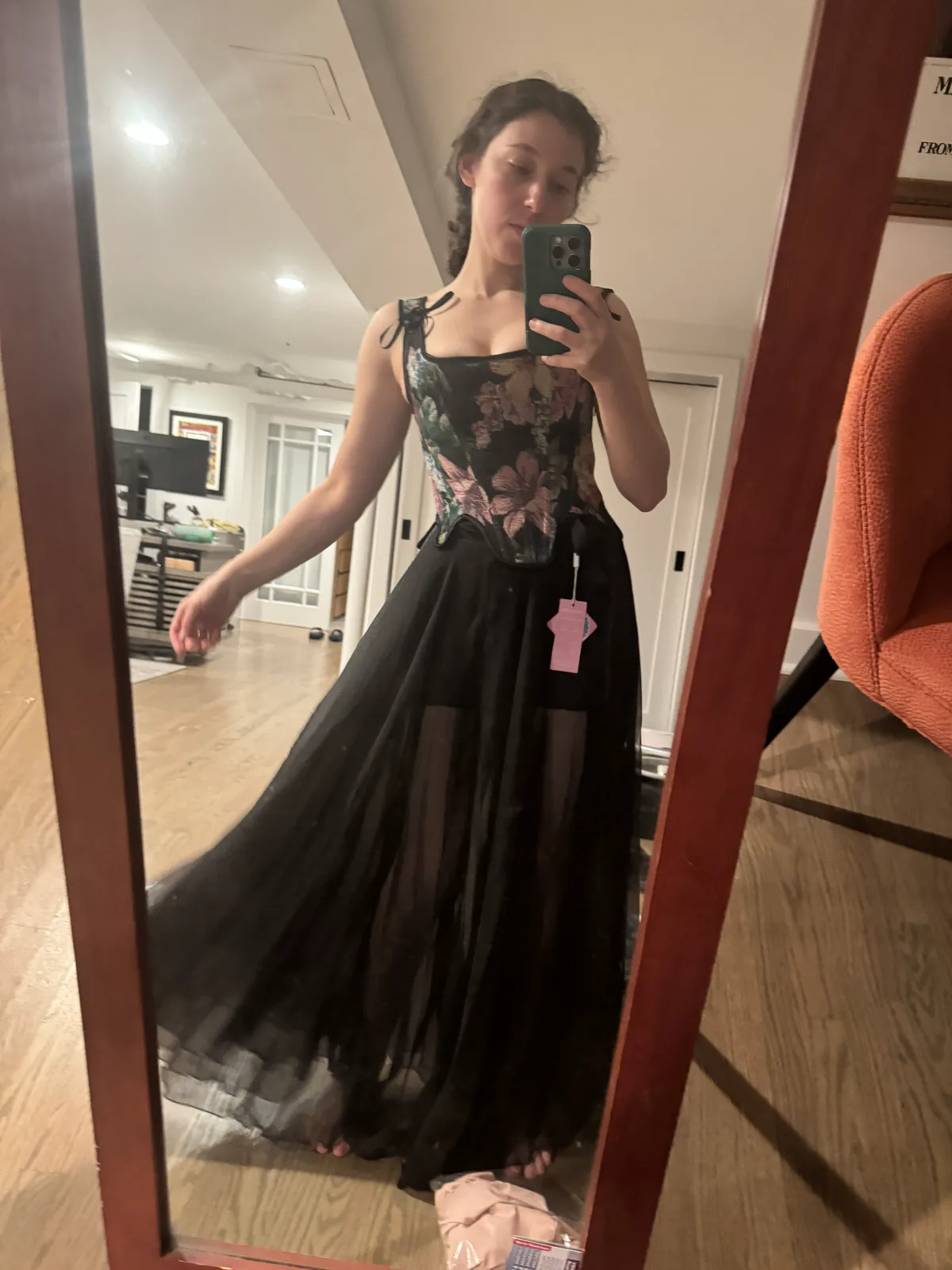 Mirror selfie holding out a long black tulle skirt worn with a floral black corset.